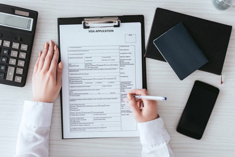 top view of woman holding pen near document with visa application lettering near smartphone with